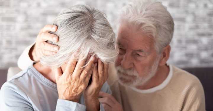 An Older Man Gently Comforts A Distressed Older Woman Who Is Crying With Her Face In Her Hands.